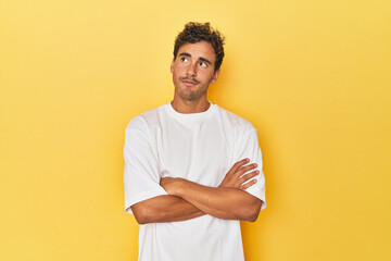 Young Latino man posing on yellow background dreaming of achieving goals and purposes