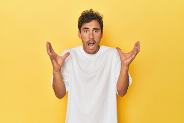 Young Latino man posing on yellow background screaming to the sky, looking up, frustrated.