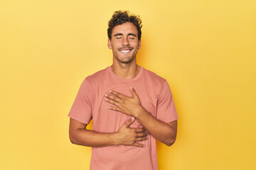 Young Latino man posing on yellow background laughs happily and has fun keeping hands on stomach.