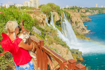 woman cradles her cat at Duden Waterfalls in Antalya, Turkey. Dramatic backdrop of both Upper and...