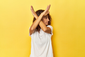 Middle-aged woman on a yellow backdrop keeping two arms crossed, denial concept.