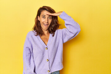 Fototapeta premium Middle-aged woman on a yellow backdrop shouts loud, keeps eyes opened and hands tense.