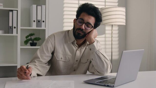 Tired exhausted weary Arabian Indian businessman bored employee designer sad sleepy unproductive at modern office work with laptop computer project boring burnout apathy business man lazy write notes