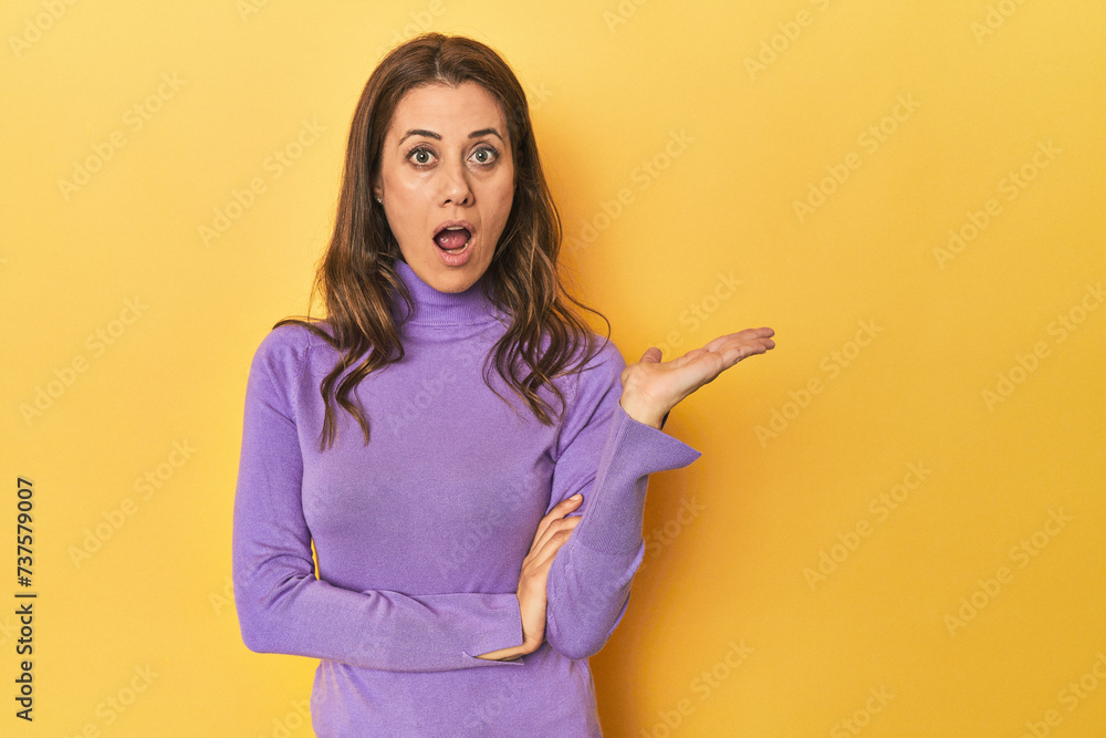 Wall mural middle-aged caucasian woman on yellow impressed holding copy space on palm.