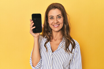 Middle aged woman using mobile phone in a yellow studio setting
