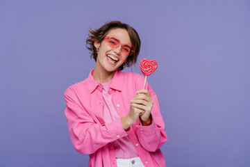 Portrait of cute smiling woman wearing pink casual clothes, holding lollipop candy