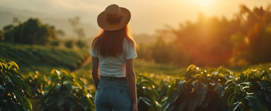 Young woman in casual attire stands amidst a lush field at sunset, contemplating nature