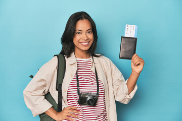 Filipina with camera, tickets, backpack on blue showing a copy space on a palm and holding another...