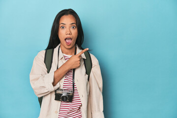 Filipina woman with camera and backpack on bluepointing to the side