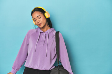 Filipina athlete in sweatshirt listening to music on blue studio