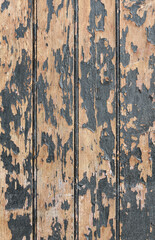 Vertical photo of an old wooden boards painted with dark paint, which has partially peeled off due to time and weather conditions