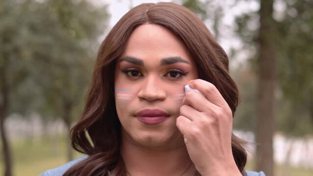 Trans woman painting her face with trans flag. Close-up view. LGBT concept.