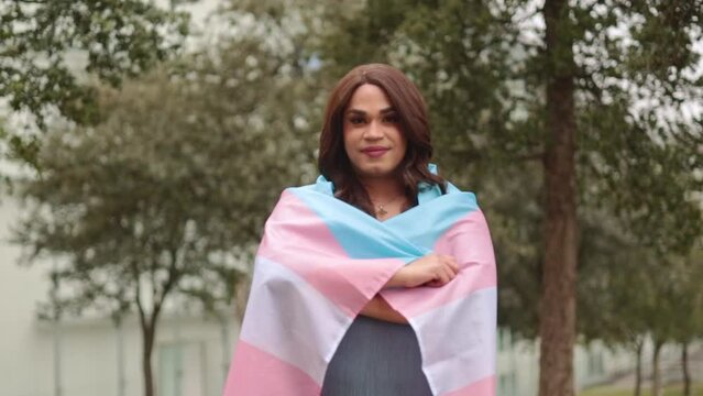 Trans woman standing with trans flag. Proud and happy expression.