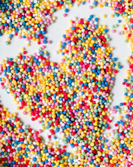 Creative flat lay composition, heart shape punctuated with candy sprinkles and white background. Realistic aesthetics. Contemporary style.