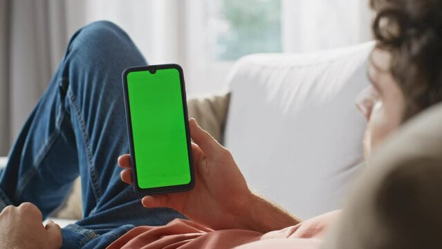 Man hands watching greenscreen cellphone at sofa closeup. Guy holding smartphone