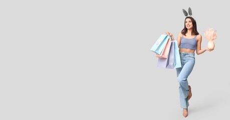 Beautiful young woman with bunny ears, gift and shopping bags on light background with space for text. Easter sale