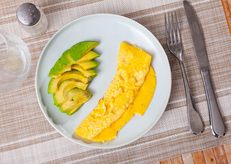 Light and hearty breakfast is served in restaurant - delicate omelette and half avocado fruit, cut into slices