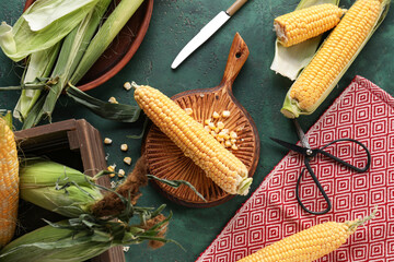 Wooden board and bowl with fresh corn cobs on green table