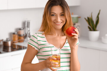 Young woman with glass of juice and apple in kitchen