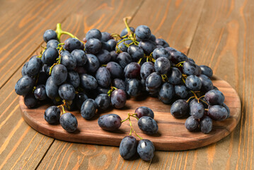 Board with sweet black grapes on wooden background