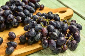 Board with sweet black grapes on green wooden background