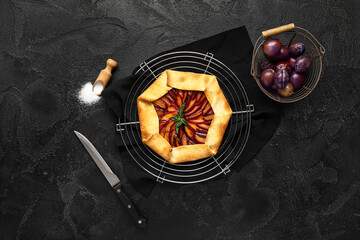 Stand with delicious plum galette and mint on black background