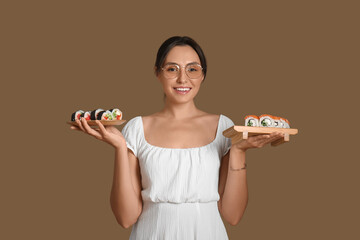 Pretty young woman with different sushi on brown background