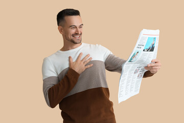 Happy young man reading newspaper on beige background