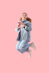 Young woman with ribbon jumping on pink background. Breast cancer awareness concept