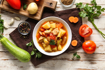 Bowl with delicious beef stew and ingredients on white wooden background