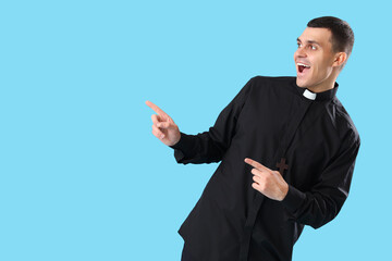 Young priest pointing at something on blue background