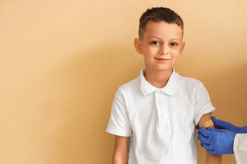 Little boy receiving plaster from doctor after vaccination on beige background