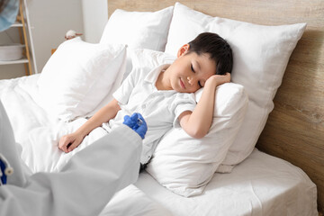 Ill little Asian boy and doctor with thermometer in bedroom