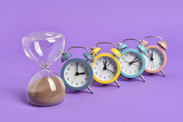 Different alarm clocks and hourglass on color background. Concept of uniqueness