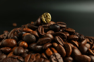 One golden coffee bean among brown ones on dark background. Concept of uniqueness