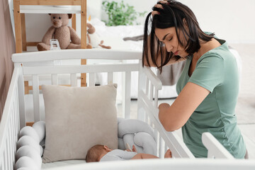 Young woman with her baby in crib suffering from postnatal depression at home