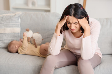 Angry young woman with her baby suffering from postnatal depression on sofa at home