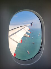 View of giant aircraft wing and cargo ships below, as seen from an airplane window (Airbus A380) - Singapore