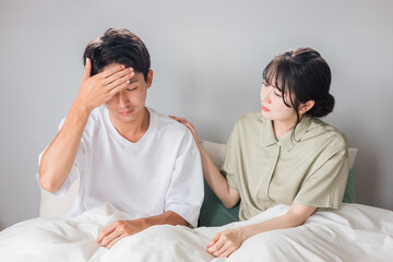 朝寝室で頭痛・発熱に悩む男性と心配する女性・夫婦・カップル
