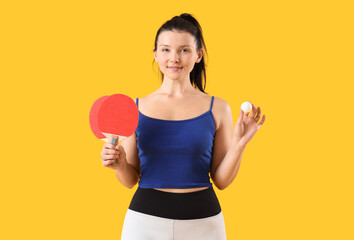Sporty young woman with ping pong rackets and ball on yellow background