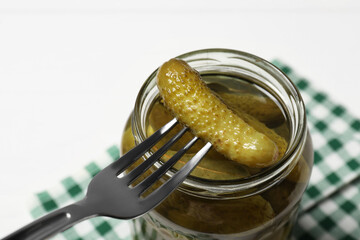 Fork with pickled cucumber over jar on white table, closeup