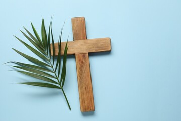 Wooden cross and palm leaf on light blue background, top view with space for text. Easter attributes