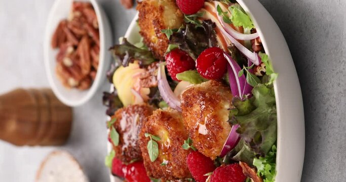 Fried goat cheese salad with raspberries and red onion and green salad, vertical video, pouring olive oil over