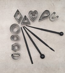 Metal cutters of different shapes and black clay tools on fan position, gray cement background