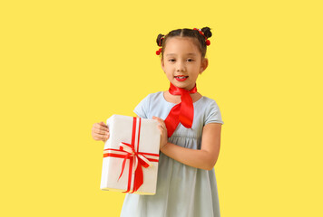 Cute little Asian girl with gift box on yellow background. Chinese New Year celebration