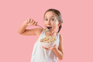 Cute little girl eating cereal rings on pink background