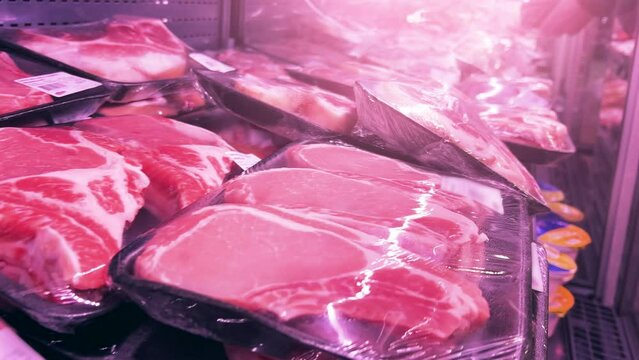 Chilled pork steaks and fillet in plastic containers covered with cling-wrap in a supermarket fridge. Close-up shot