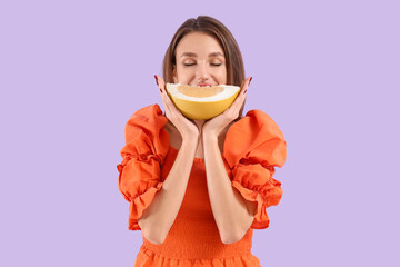 Young woman with pomelo slice on lilac background