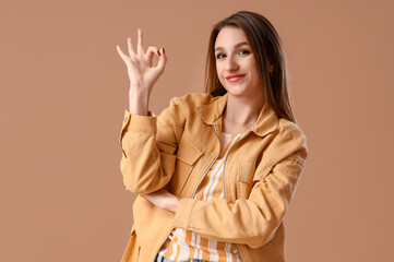 Young woman showing OK on brown background