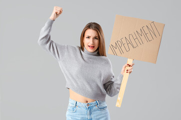 Protesting young woman holding placard with word IMPEACHMENT on light background